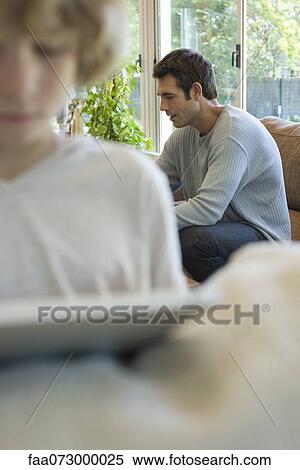 Man sitting on sofa in living room View Large Photo Image Stock Photography - Man sitting on sofa in living room. Fotosearch