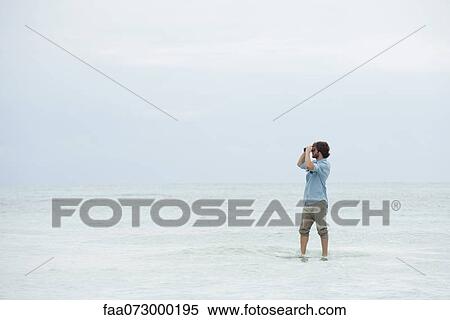 Man standing in sea, looking through binoculars View Large Photo Image Stock Photography - Man standing in sea, looking through binoculars. Fotosearch