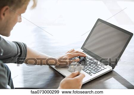 Stock Photo - Man using credit card to make an online purchase. Fotosearch