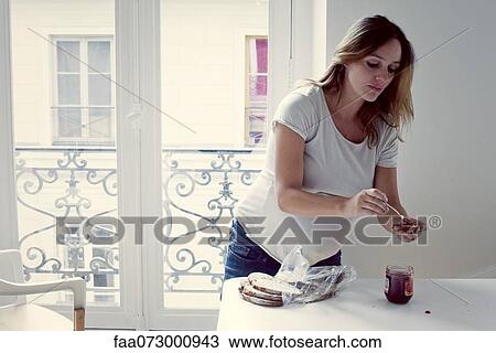 Stock Image - Mid-adult woman spreading jam on toast. Fotosearch