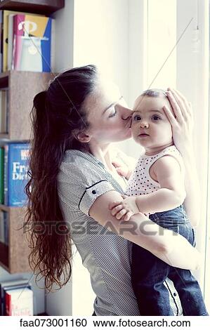Stock Image - Mother kissing baby girl, portrait. Fotosearch