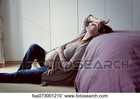 Stock Image - Pregnant woman leaning against bed relaxing. Fotosearch