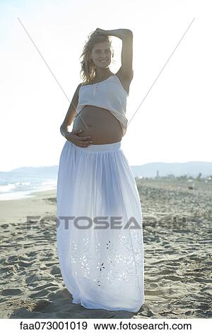 Pregnant woman standing on beach with hand on belly View Large Photo Image Stock Photo - Pregnant woman standing on beach with hand on belly. Fotosearch