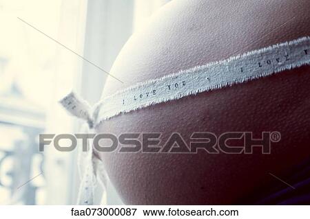 Pregnant woman with ribbon wrapping around stomach, mid section View Large Photo Image Stock Photo - Pregnant woman with ribbon wrapping around stomach, mid section. Fotosearch