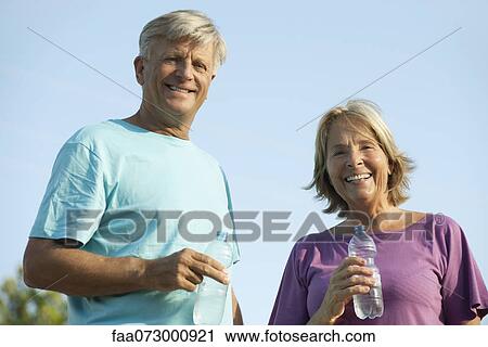 Stock Image - Senior couple holding bottles of water, portrait. Fotosearch