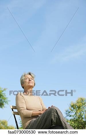 Senior woman sitting outdoors enjoying warmth of sun View Large Photo Image Stock Image - Senior woman sitting outdoors enjoying warmth of sun. Fotosearch