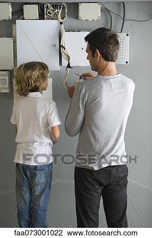 Stock Image - Son watching father fixing wires. Fotosearch