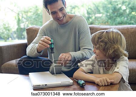 Stock Photo - Son watching father repairing laptop computer. Fotosearch