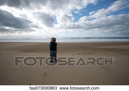 Stock Image - Toddler walking on beach, rear view. Fotosearch