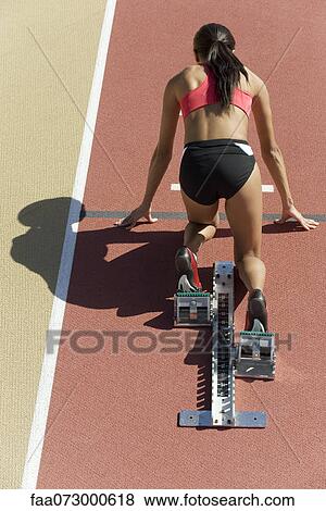 Stock Photo - Woman crouched in starting position on running track, rear view. Fotosearch
