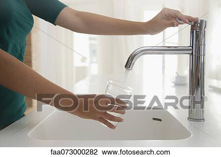 Woman filling glass of water at kitchen sink, cropped View Large Photo Image Stock Image - Woman filling glass of water at kitchen sink, cropped. Fotosearch