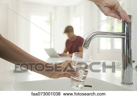 Woman filling glass of water at kitchen sink, cropped View Large Photo Image Stock Photo - Woman filling glass of water at kitchen sink, cropped. Fotosearch