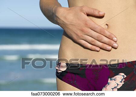 Stock Photograph - Woman in bikini bottom, hand on abdomen, mid section. Fotosearch