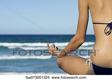 Woman in bikini sitting in lotus position by sea, rear view View Large Photo Image Picture - Woman in bikini sitting in lotus position by sea, rear view. Fotosearch