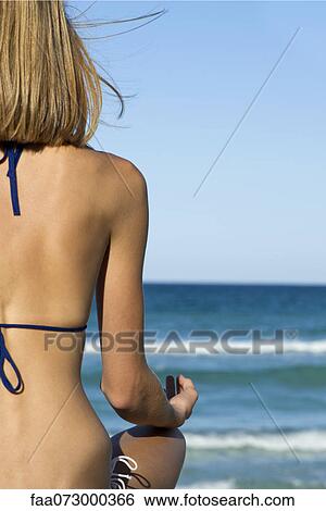 Stock Photograph - Woman in bikini sitting in lotus position, rear view. Fotosearch