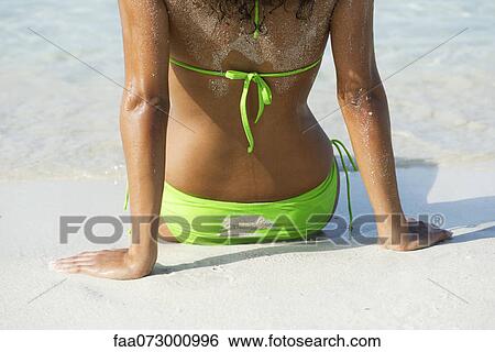 Woman in bikini sitting on beach, rear view, mid section View Large Photo Image Stock Photograph - Woman in bikini sitting on beach, rear view, mid section. Fotosearch