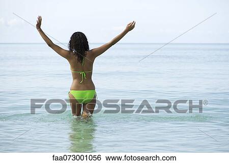 Woman in bikini standing in ocean with arms out, rear view View Large Photo Image Stock Photograph - Woman in bikini standing in ocean with arms out, rear view. Fotosearch