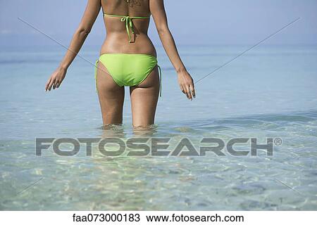 Stock Image - Woman in bikini standing in water, mid section. Fotosearch