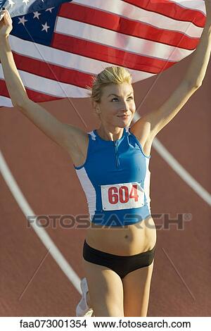Picture - Woman running on track with American flag. Fotosearch