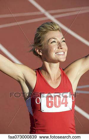 Stock Photo - Woman running on track with arms raised in victory. Fotosearch