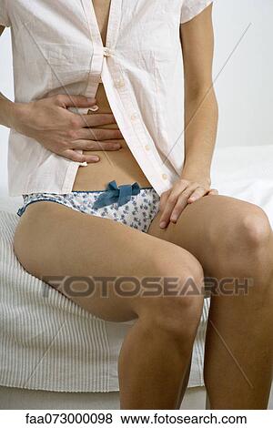 Woman sitting on bed, hand on stomach View Large Photo Image Stock Photo - Woman sitting on bed, hand on stomach. Fotosearch