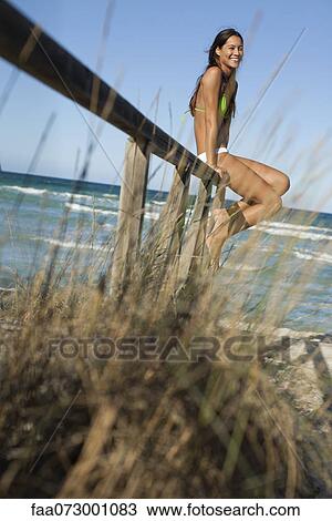 Stock Image - Woman sitting on railing at the beach. Fotosearch
