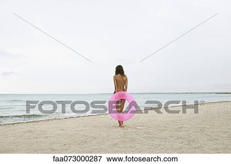 Woman standing on beach, holding inflatable ring, rear view View Large Photo Image Stock Photo - Woman standing on beach, holding inflatable ring, rear view. Fotosearch