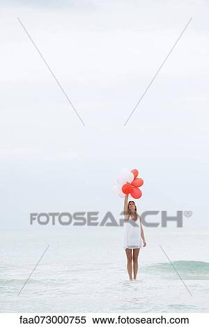 Woman standing on surface of water, holding bunch of balloons View Large Photo Image Stock Photography - Woman standing on surface of water, holding bunch of balloons. Fotosearch