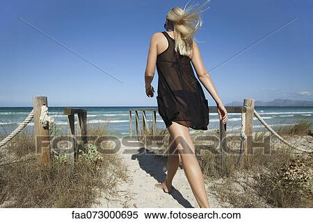 Woman walking on beach path toward sea, rear view View Large Photo Image Stock Photography - Woman walking on beach path toward sea, rear view. Fotosearch