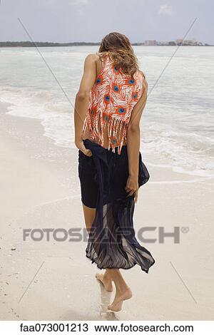 Stock Image - Woman walking on beach, rear view. Fotosearch