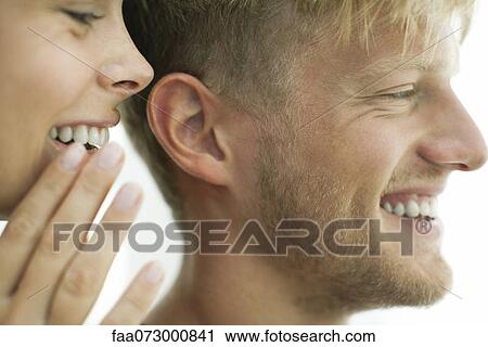 Stock Image - Woman whispering in man's ear, close-up. Fotosearch