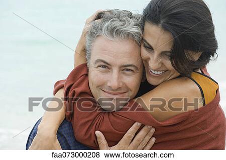 Stock Photo - Woman wrapping arms around husband, portrait. Fotosearch