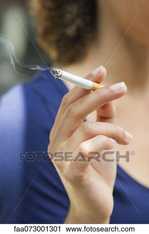 Stock Image - Woman's hand holding lit cigarette. Fotosearch