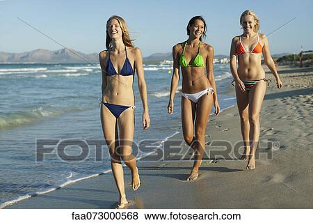 Stock Photo - Women in bikinis walking on beach. Fotosearch