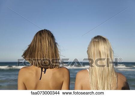 Women side by side at the beach, looking at sea, rear view View Large Photo Image Picture - Women side by side at the beach, looking at sea, rear view. Fotosearch