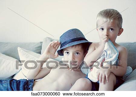 Stock Image - Young brothers together on sofa, portrait. Fotosearch