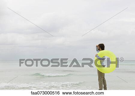Young man carrying swimming ring, looking into distance View Large Photo Image Stock Photograph - Young man carrying swimming ring, looking into distance. Fotosearch