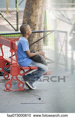 Young man sitting on bench View Large Photo Image Stock Image - Young man sitting on bench. Fotosearch