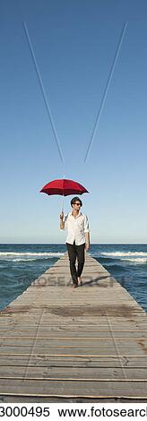 Stock Photography - Young man walking on pier with umbrella. Fotosearch