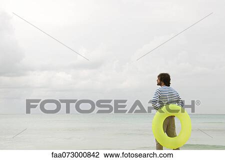 Young man with inflatable ring, looking at ocean view View Large Photo Image Stock Image - Young man with inflatable ring, looking at ocean view. Fotosearch