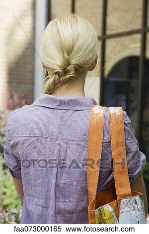 Stock Photography - Young woman carrying shoulder bag, rear view. Fotosearch