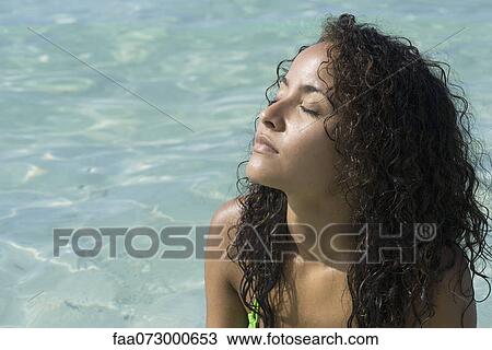 Stock Image - Young woman enjoying warmth of sun with eyes closed, portrait. Fotosearch