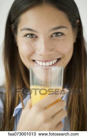 Stock Image - Young woman holding glass of orange juice. Fotosearch