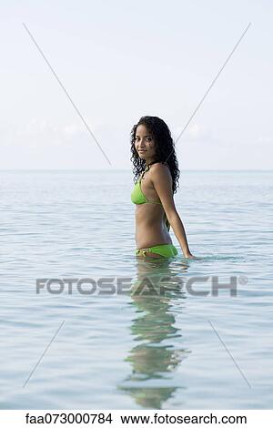 Young woman in bikini standing waist deep in water, portrait View Large Photo Image Picture - Young woman in bikini standing waist deep in water, portrait. Fotosearch