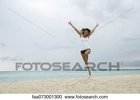 Stock Image - Young woman jumping in air on beach. Fotosearch