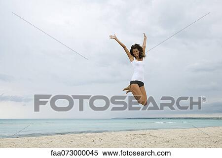 Stock Photography - Young woman jumping in air on beach. Fotosearch