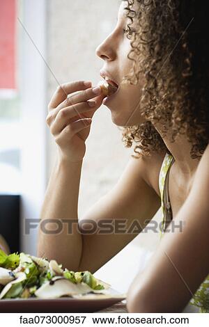 Stock Photo - Young woman with curly hair eating salad, side view. Fotosearch