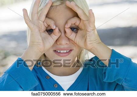 Stock Photograph - Boy forming circles with fingers around eyes. Fotosearch