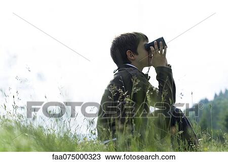 Boy sitting in meadow looking through binoculars View Large Photo Image Stock Image - Boy sitting in meadow looking through binoculars. Fotosearch