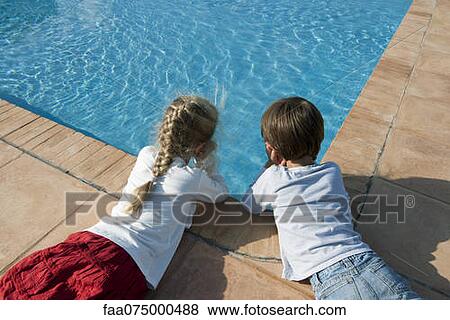Stock Photo - Children lying beside swimming pool, gazing at water. Fotosearch